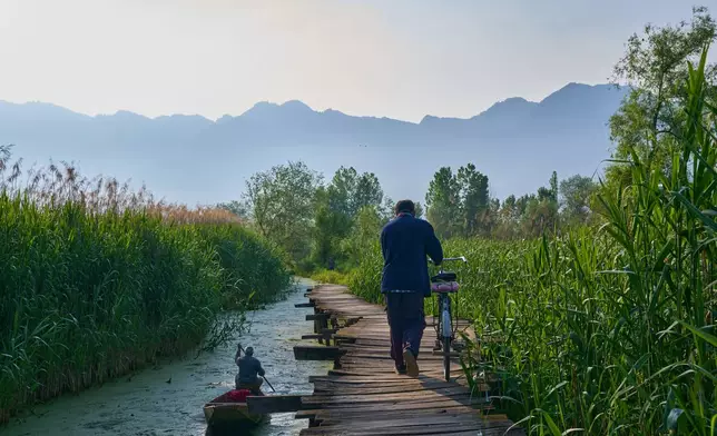 A cyclist walks a bike on a wooden footbridge as a man rows his boat in the interiors of Dal Lake on the outskirts of Srinagar, Indian controlled Kashmir, Monday, May 4, 2026. (AP Photo/Dar Yasin)