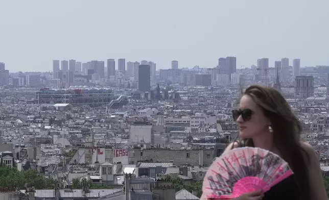 A woman holds a fan as the roofs of Paris are seen background, Tuesday, June 23, 2026. (AP Photo/John Leicester)