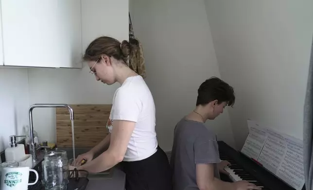 Amelie Kenney, right, plays piano in the attic apartment she shares with her partner Francesca Pilia, in Paris, Wednesday, June 24, 2026. (AP Photo/John Leicester)
