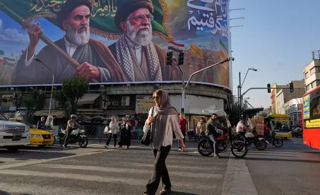 People walk under a banner showing portraits of the late revolutionary founder Ayatollah Khomeini, left, and the slain Supreme Leader Ayatollah Ali Khamenei, who was killed in U.S. and Israeli strikes on Feb. 28, in Tehran, Iran, Saturday, June 6, 2026. (AP Photo/Vahid Salemi)