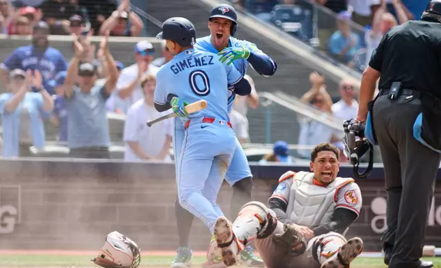 Toronto Blue Jays' Andrés Giménez (0) celebrates with George Springer, second from left, after scoring on a single hit by Nathan Lukes (not shown) against the Baltimore Orioles during sixth-inning baseball game action in Toronto, Sunday, June 7, 2026. (Sammy Kogan/The Canadian Press via AP)