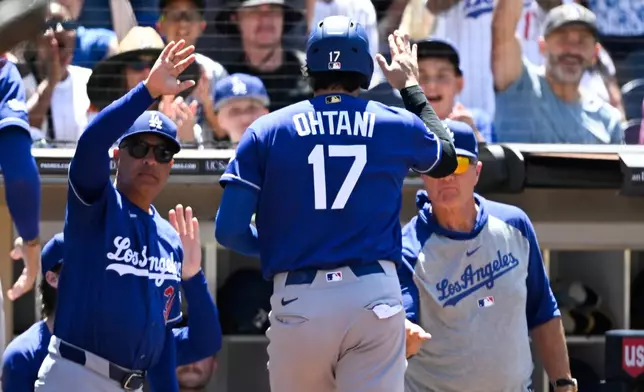 Los Angeles Dodgers designated hitter Shohei Ohtani (17) is welcomed into the dugout after scoring during the fifth inning of a baseball game against the San Diego Padres, Sunday, June 28, 2026, in San Diego. (AP Photo/Denis Poroy)