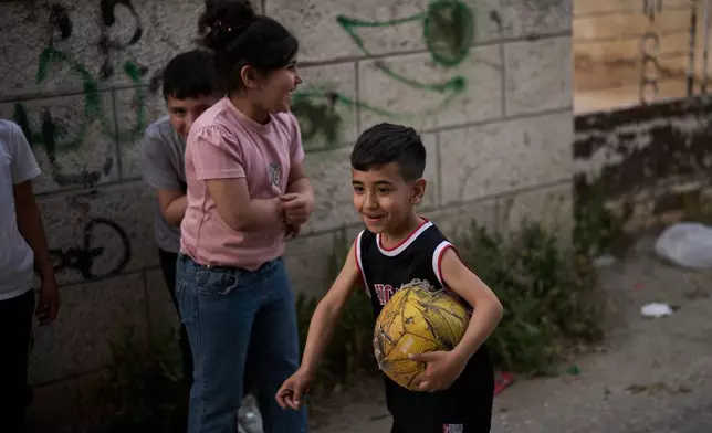 A Palestinian boy carries a worn soccer ball while playing with friends in an alley in the West Bank town of Al-Ram, Monday, May 11, 2026. (AP Photo/Leo Correa)