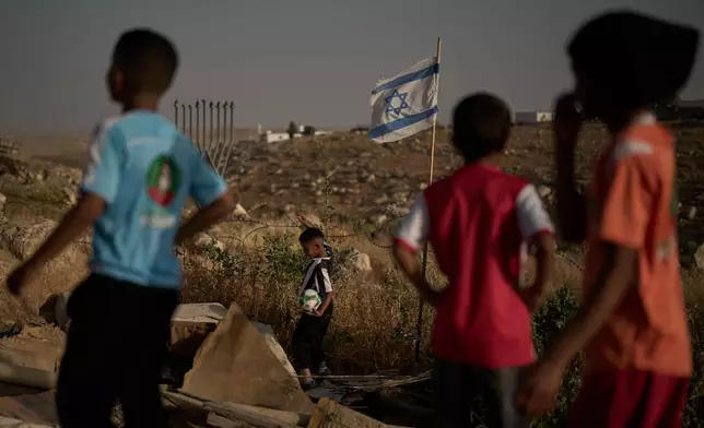 A Palestinian boy retrieves a soccer ball after it landed beyond a barbed-wire fence erected by Israeli settlers next to a football pitch in the West Bank Bedouin village of Umm al-Khair, Tuesday, May 12, 2026. (AP Photo/Leo Correa)