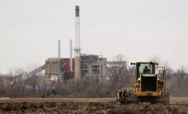 FILE - A worker prepares a plot of land for an AI data center, with a retired power plant being refurbished to provide electricity for the facility in the distance, March 24, 2026, in Independence, Mo. (AP Photo/Charlie Riedel)