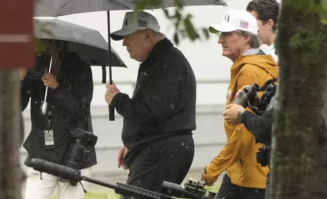 President Donald Trump walks carrying an umbrella alongside Interior Secretary Doug Burgum, right, at East Potomac Park golf course, Sunday, June 28, 2026, in Washington. (AP Photo/Mark Schiefelbein)