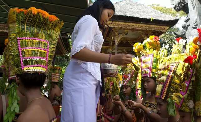 A religious volunteer, locally called "ngayah" gives blessing to dancers before performing the sacred Rejang dance during Kuningan holiday, which marks the end of the 10-day Galungan festival celebrating the victory of good over evil, in Karangasem, Bali, Indonesia, Saturday, June 27, 2026. (AP Photo/Firdia Lisnawati)