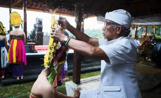 A Hindu priest puts incense stick on the headwear of a dancer to bless her before performing the sacred Rejang dance during Kuningan holiday, which marks the end of the 10-day Galungan festival celebrating the victory of good over evil, in Karangasem, Bali, Indonesia, Saturday, June 27, 2026. (AP Photo/Firdia Lisnawati)