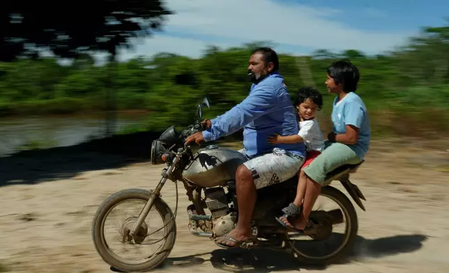Cowboy Leandro Rui Araujo, known as Bodo, rides a motorcycle with sons Davi and Guido in Boa Esperanca village of the Javae Indigenous group on Bananal Island in Formoso do Araguaia, Tocantins state, Brazil, Friday, May 22, 2026. (AP Photo/Andre Penner)