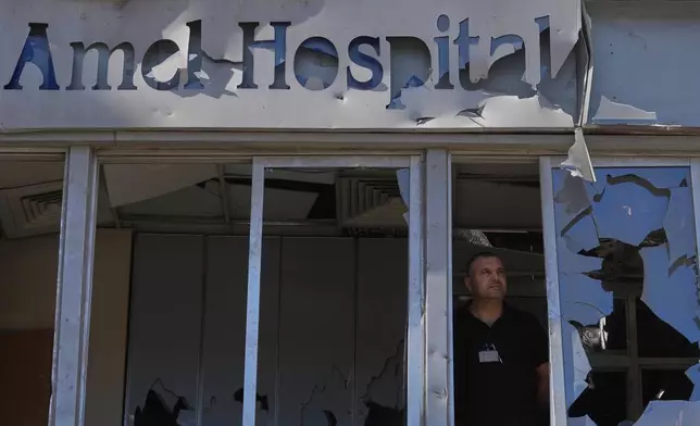 A man stands behind shattered windows at Jabal Amel Hospital, which was heavily damaged in Israeli strikes that hit nearby buildings earlier this month, in the southern port city of Tyre, Lebanon, Thursday, June 18, 2026. (AP Photo/Hassan Ammar)