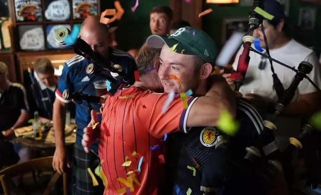 Scotland soccer fans with bagpipes embrace amid confetti after playing together at the Ball and Chain music bar before the Tartan Army marches to a Miami Marlins against the Texas Rangers baseball game in Miami, Monday, June 22, 2026. (AP Photo/Rebecca Blackwell)