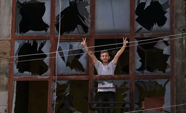 A man flashes the victory sign through the shattered window of a damaged apartment following a ceasefire between Israel and Hezbollah in the town of Nabatiyeh, southern Lebanon, Monday, June 22, 2026. (AP Photo/Mohammed Zaatari)