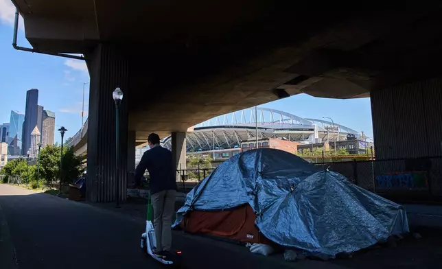 Seattle Stadium is seen in the background as a person rides a scooter past a series of tents on a trail near the stadium ahead of the 2026 FIFA World Cup soccer matches Wednesday, May 27, 2026, in downtown Seattle. (AP Photo/Lindsey Wasson)