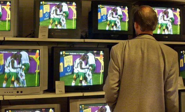 FILE - A man watches the celebrations of Senegal's soccer players during the opening match France vs. Senegal of the soccer World Championships in South Korea on a wall of TV screens in a department store in downtown Hamburg, northern Germany, May 31, 2002. (AP Photo/Kirstin Knorr, File)