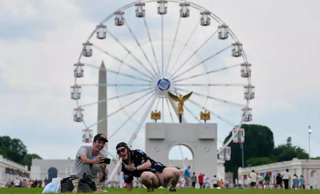 Christine Bayly, right, and Jason Brown, left, take a photo as they eat lunch on the National Mall with the Washington Monument, Freedom 250 Ferris Wheel, and a replica of the triumphal arch, behind them during the Great American State Fair, Friday, June 26, 2026, in Washington. (AP Photo/Carolyn Kaster)