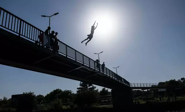 Young men jump from a bridge into a river, in Lille, northern France, Wednesday June 24, 2026. (AP Photo/Jean-Francois Badias)