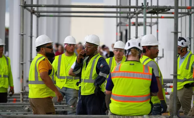Workers wait for the rain to stop before resuming work to remove President Donald Trump's name from the John F. Kennedy Center for the Performing Arts in Washington, Friday, June 12, 2026. (AP Photo/Cliff Owen)