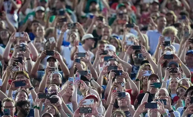 Fans hold their cell phones during the World Cup Group J soccer match between Algeria and Austria in Kansas City, Mo., Saturday, June 27, 2026. (AP Photo/Charlie Riedel)