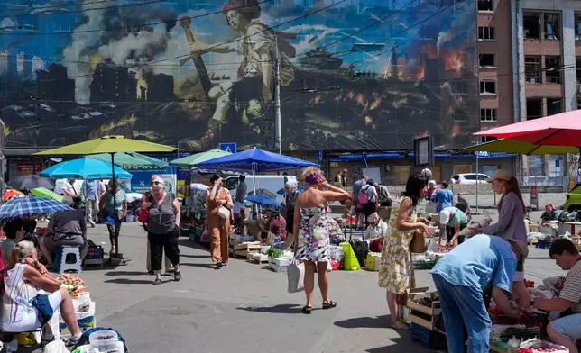 People buy food at an improvised outdoor market surrounded by damaged buildings covered with street artist paintings close to a big city marketplace that was ruined recently by Russian missiles in Kyiv, Ukraine, Monday, June 22, 2026. (AP Photo/Efrem Lukatsky)