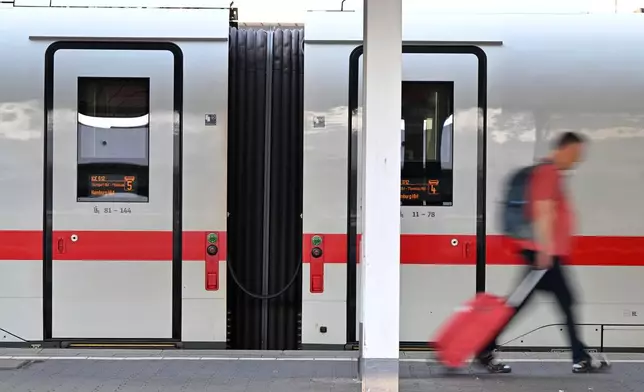 A passenger walks past an ICE train at Munich Central Station in Munich, Germany Wednesday, June 24, 2026, following the nationwide service disruption on the Deutsche Bahn network. (Peter Kneffel/dpa via AP)