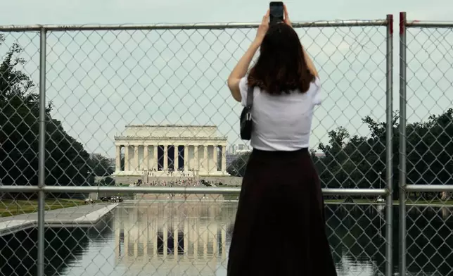 A person holds a cell phone high to take a photo of the Lincoln Memorial Reflecting Pool and the Lincoln Memorial from behind a chain link fence Friday, June 26, 2026, in Washington. (AP Photo/Carolyn Kaster)