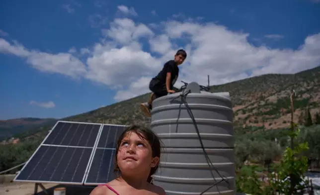 A girl looks toward what residents said was an Israeli drone flying overhead as a boy checks his family's water storage tank in Halta, southern Lebanon, Friday, June 12, 2026. (AP Photo/Hassan Ammar)