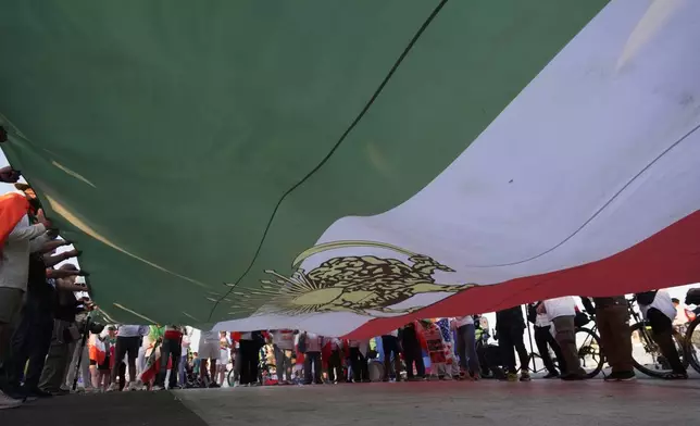 People unfurl a large Pre-revolutionary Iranian flag during a protest outside Los Angeles Stadium before the World Cup Group G soccer match between Iran and New Zealand in Inglewood, Calif., near Los Angeles, Monday, June 15, 2026. (AP Photo/Ty ONeil)