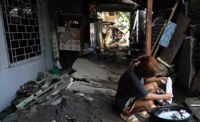 A woman washes clothes along a damaged pathway in General Santos, southern Philippines, Thursday, June 11, 2026, following Monday's powerful earthquake. (AP Photo/Basilio Sepe)