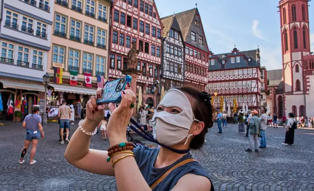 A tourist from China protects her face from the sun as she takes pictures at the Roemerberg square in Frankfurt, Germany, Saturday, June 27, 2026. (AP Photo/Michael Probst)