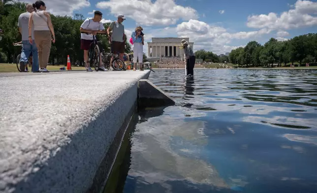 Visitors watch as a National Park Service employee uses a vacuum to clean the Lincoln Memorial Reflecting Pool near a missing section of blue coating, Friday, June 19, 2026, in Washington. (AP Photo/Mark Schiefelbein)