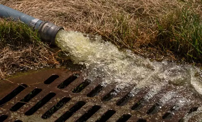 Water is pumped from a vacuum into a drain near the Lincoln Memorial Reflecting Pool, Friday, June 19, 2026, in Washington. (AP Photo/Mark Schiefelbein)