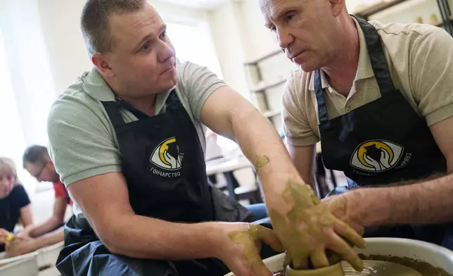 Ivan Shostak, left, a blind Ukrainian war veteran trains his blind comrade Viacheslav Sadovskyi, right, to make a clay plate on a pottery wheel in a workshop at a rehabilitation center in Vinnytsia, Ukraine, on May 21, 2026. (AP Photo/Evgeniy Maloletka)