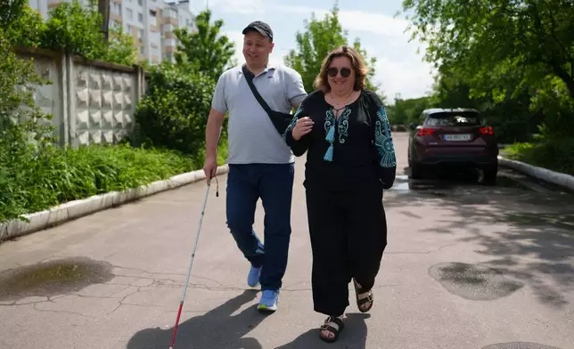 Ivan Shostak, left, a blind Ukrainian war veteran and Anastasia Lanina, community development officer of UNDP walk on a street in Vinnytsia, Ukraine, on May 21, 2026. (AP Photo/Evgeniy Maloletka)