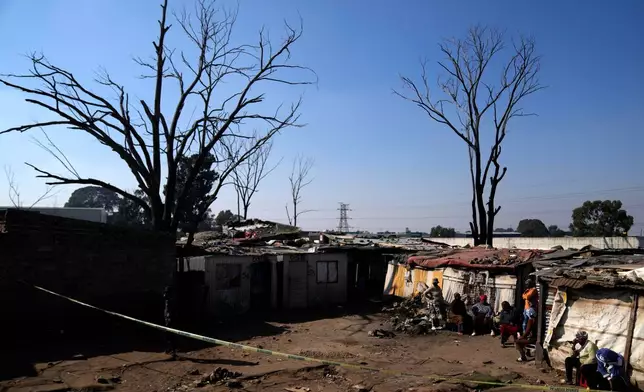 People sit outside a cordon, at the scene of a mass shooting at an informal settlement in the Cleveland suburb of Johannesburg, South Africa, Wednesday, June 10, 2026. (AP Photo/Themba Hadebe)