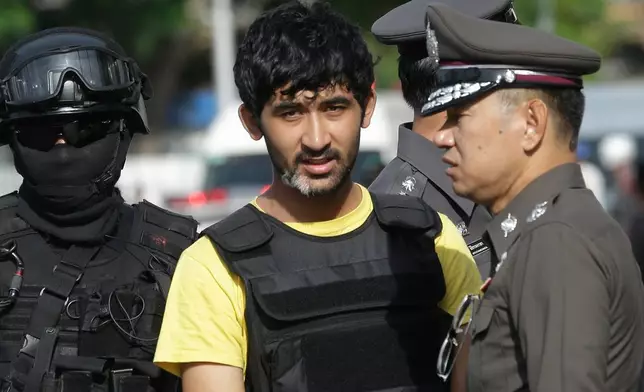 FILE - Police officers escort Yusufu Mieraili, yellow shirt, outside Hua Lamphong railway station in Bangkok, on Sept. 9, 2015. (AP Photo/Sakchai Lalit, File)