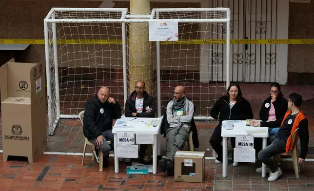Election officials wait for voters during the runoff presidential election in Bogota, Colombia, Sunday, June 21, 2026. (AP Photo/Fernando Vergara)