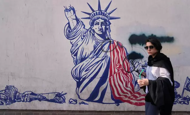 A woman walks past an anti-American mural on the wall of the former U.S. Embassy, now a museum, in Tehran, Iran, Friday, June 12, 2026. (AP Photo/Vahid Salemi)