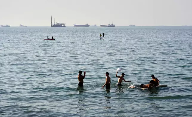 Residents swim and play in the waters of the Strait of Hormuz while cargo ships and commercial vessels lie anchored in the distance off Bandar Abbas, Iran, Wednesday, June 10, 2026.(Razieh Poudat/ISNA via AP)