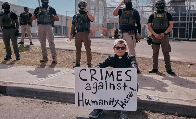 A protester holds a sign as ICE agents stand guard outside the Delaney Hall detention during a protest against the transfer of detainees on Tuesday, May 26, 2026, in Newark, N.J. (AP Photo/Andres Kudacki)