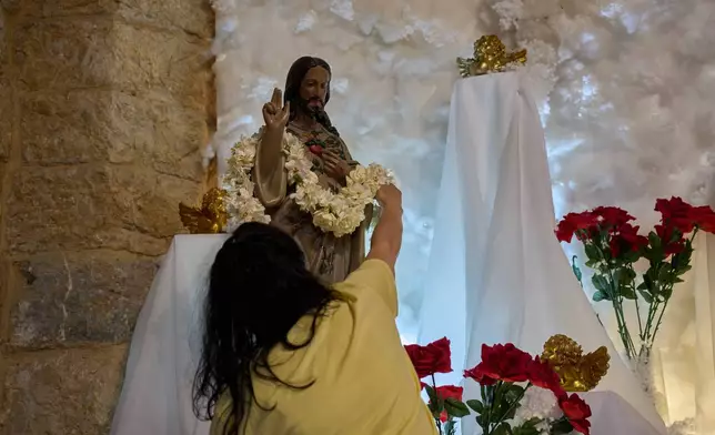 A woman places a flower garland on a statue of Jesus Christ inside St. Georges Church in the southern village of Qlayaa, Lebanon, Wednesday, June 10, 2026. (AP Photo/Hassan Ammar)