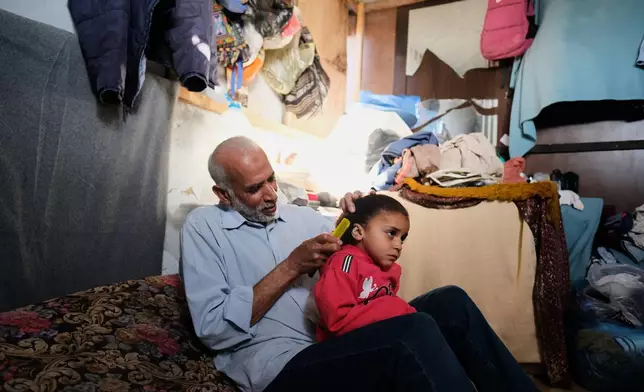 Mahmoud Nofal, 64, combs the hair of his three-year-old granddaughter, Raneen Nofal, whom he has raised since her parents were killed in an Israeli airstrike, in Khan Younis, Thursday, April 30, 2026. (AP Photo/Jehad Alshrafi)