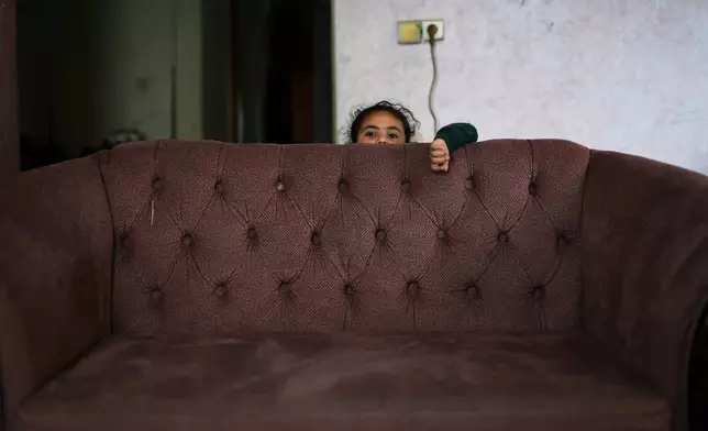 Habiba al-Kafarna, 5, who was orphaned when her parents, Ahmed and Sajida, were killed in an Israeli strike on a school sheltering displaced people in 2025, stands behind a sofa in the Gaza City home where she lives, May 31, 2026. (AP Photo/Abdel Kareem Hana)