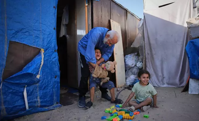 Mahmoud Nofal, 64, plays with his grandchildren, Tamim and Ranin Nofal, whom he has raised since their parents were killed in an Israeli airstrike, outside their tent in Khan Younis, southern Gaza Strip, June 2, 2026. (AP Photo/Abdel Kareem Hana)