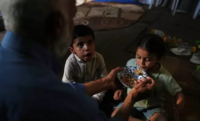 Mahmoud Nofal, 64, feeds his grandchildren, Tamim and Raneen Nofal, whom he has raised since their parents were killed in an Israeli airstrike, in Khan Younis, southern Gaza Strip, June 2, 2026. (AP Photo/Abdel Kareem Hana)