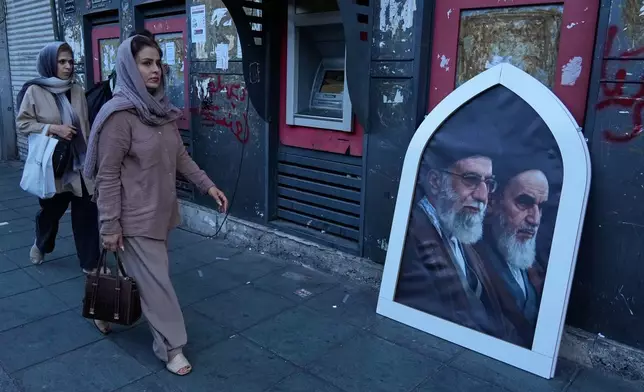 Pedestrians walk past a poster showing the slain Iranian Supreme Leader Ayatollah Ali Khamenei, left, and the late revolutionary founder Ayatollah Khomeini on a sidewalk at the Islamic Revolution square in Tehran, Iran, Sunday, June 14, 2026. (AP Photo/Vahid Salemi)
