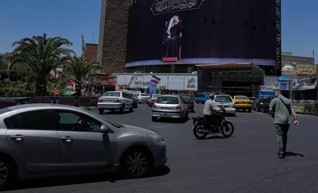 People pass under a billboard showing a portrait of the slain Iranian Supreme Leader Ayatollah Ali Khamenei, who was killed in U.S. and Israeli strikes on Feb. 28, in downtown Tehran, Iran, Monday, June 15, 2026. (AP Photo/Vahid Salemi)