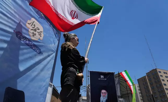 A woman waves an Iranian flag during a pro-government campaign as a portrait of the slain Supreme Leader Ayatollah Ali Khamenei, who was killed in U.S. and Israeli strikes on Feb. 28, is displayed at right, in downtown Tehran, Iran, Monday, June 15, 2026. (AP Photo/Vahid Salemi)