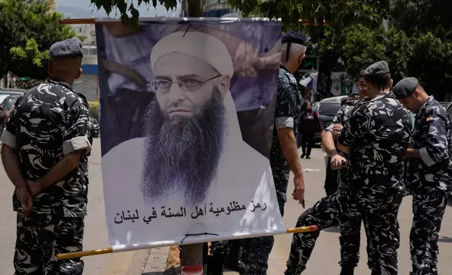 FILE - Police stand guard where a portrait of imprisoned hardline Sunni cleric Ahmad al-Assir hangs on a post, on the sidelines of a protest against a clause in a proposed amnesty law that would exclude some prisoners, including the cleric, from being eligible for amnesty, after Friday prayers in Beirut, Lebanon, Friday, May 22, 2026. (AP Photo/Bilal Hussein, File)