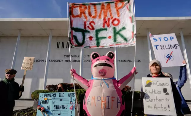 FILE - Demonstrators, including Nadine Siler, of Waldorf, Md., dressed in a pink frog costume, hold up signs at a designated protest point in front of the John F. Kennedy Memorial Center for the Performing Arts, a day after a Trump-appointed board voted to add President Donald Trump's name to the Kennedy Center, Dec. 20, 2025, in Washington. (AP Photo/Julia Demaree Nikhinson, file)