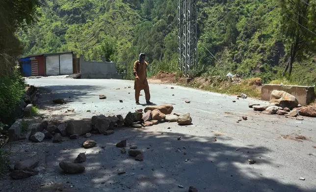 A local resident walks through a road barricaded with stones by protesters during a strike called by an outlawed alliance of activist groups "Joint Awami Action Committee" (JAAC) demanding greater political rights and the abolition of 12 legislative refugee seats, on the outskirts of Muzaffarabad, the capital of Pakistan-administered Kashmir, Tuesday, June 9, 2026. (AP Photo/M.D. Mughal)